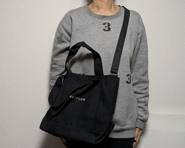 BAYFLOWトートを肩掛け・斜め掛けしている着用イメージ。グレーのスウェットにブラックバッグが映える