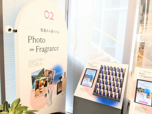 Photo→Fragranceコーナーの全景。サイネージと番号付きの青いボトルが並んでいる