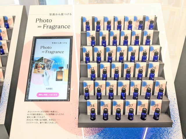 Photo→Fragranceの端末画面と、番号1〜39まで並ぶ青いサンプルボトルのコーナー