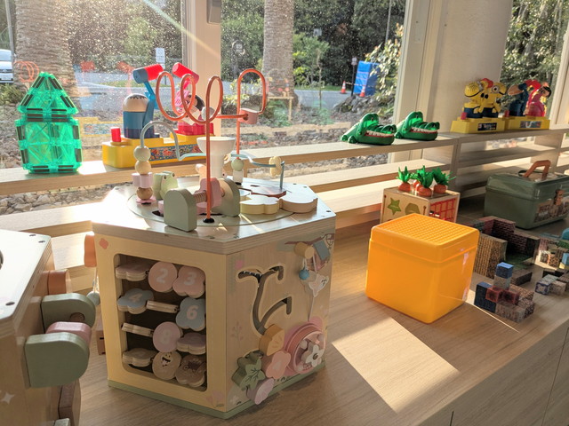 キッズスペースのおもちゃコーナーアップ。ビジーボードや積み木など幼児向けの木のおもちゃが並ぶ