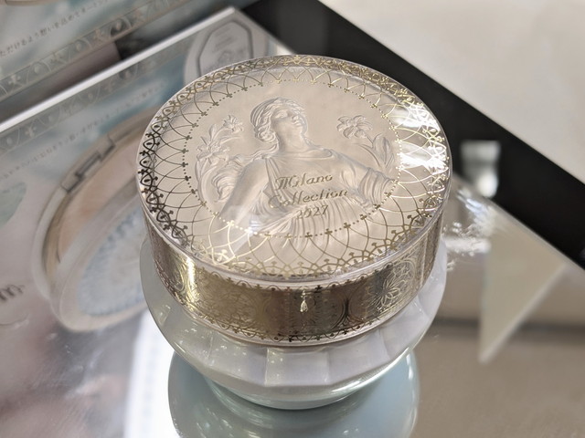 ミラノコレクション ドレスアップクリーム2027の容器アップ。蓋に女神とユリの刻印、レース調のデザインが施されている