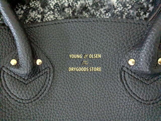 ブラックのレザー調バッグ正面の箔押しロゴアップ。YOUNG & OLSEN The DRYGOODS STOREの文字がゴールドで入っている